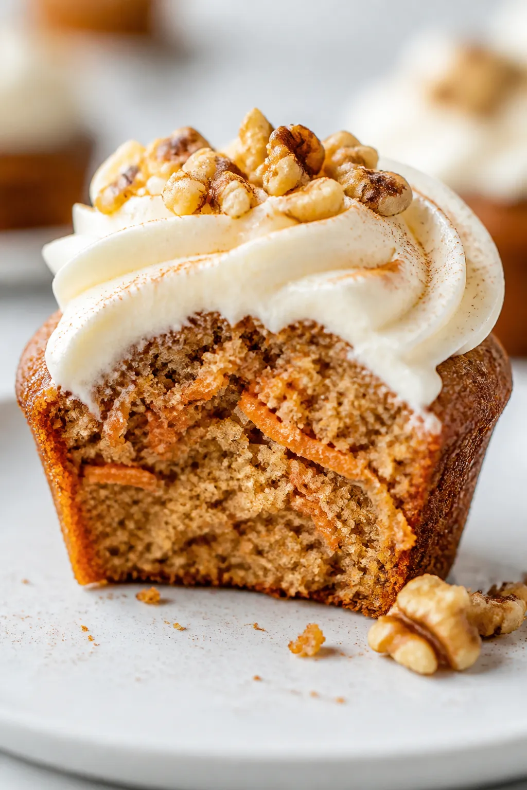 Close-up detail of a single gluten-free carrot cake muffin cut in half on a matte white plate, showi