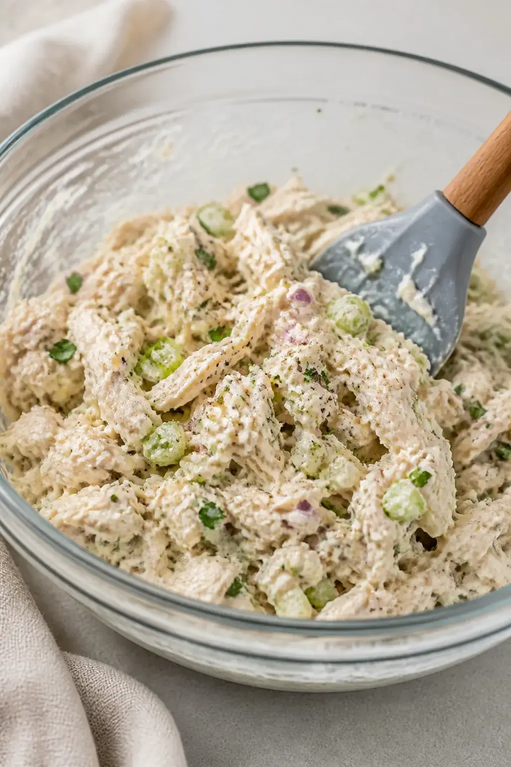 Close-up detail, process shot: A medium glass bowl of freshly mixed chicken salad made with flaked c