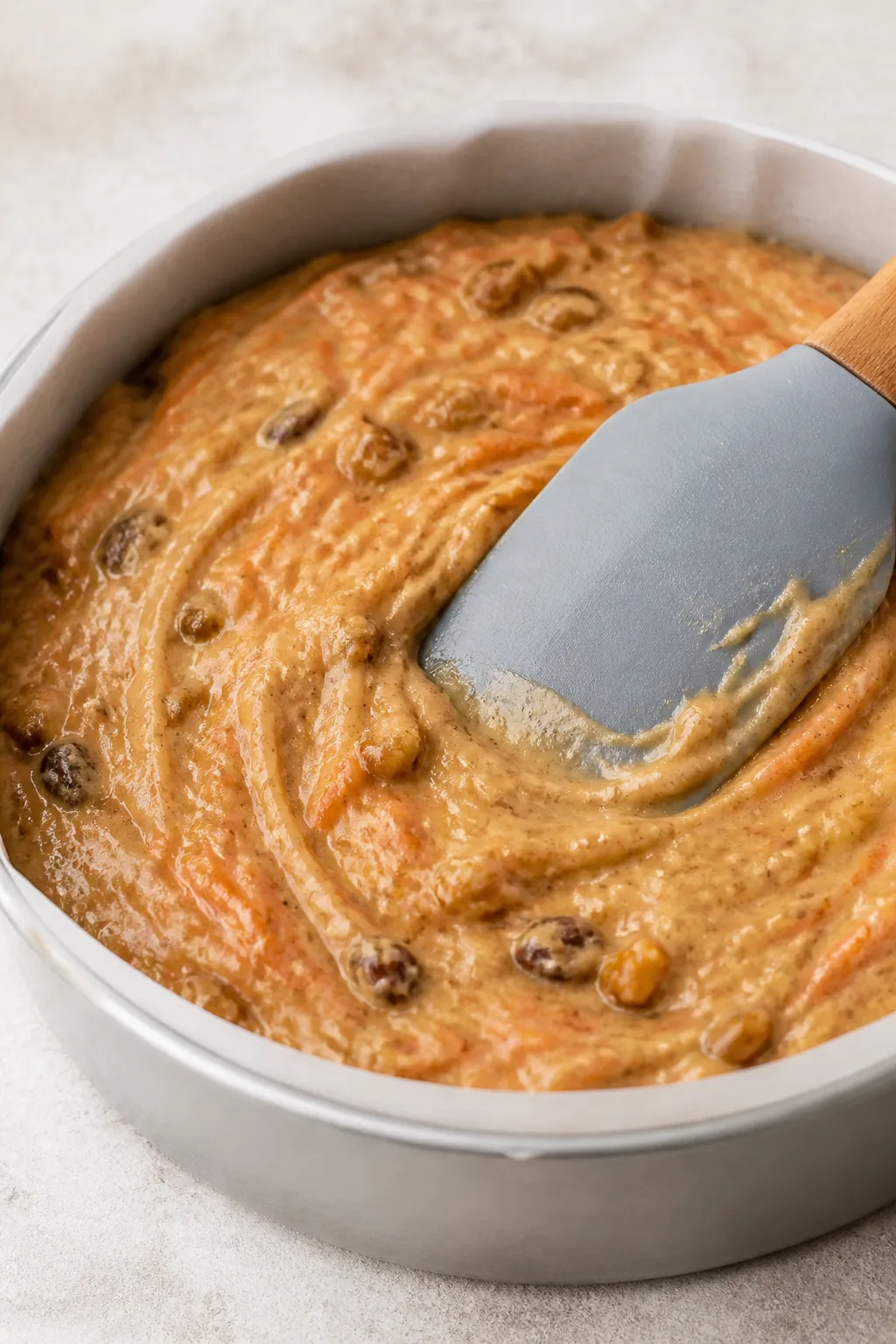 Close-up process shot of a thick carrot cake batter being spread evenly into an 8-inch round pan wit