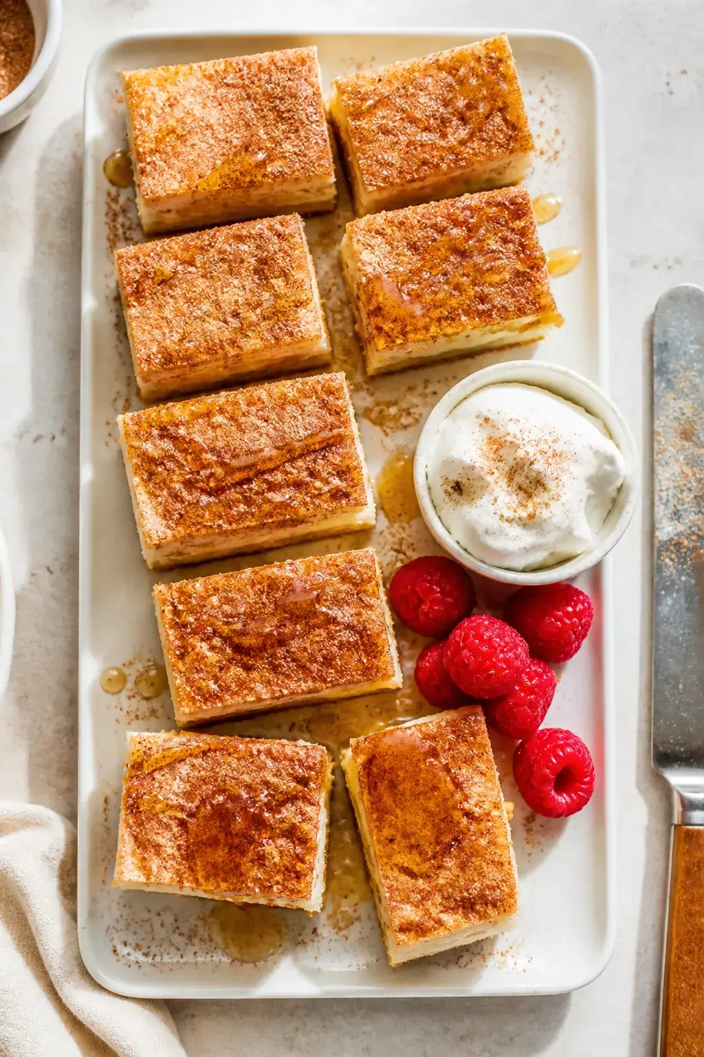 Overhead final presentation: Neatly sliced sopapilla cheesecake bars arranged on a matte white platt