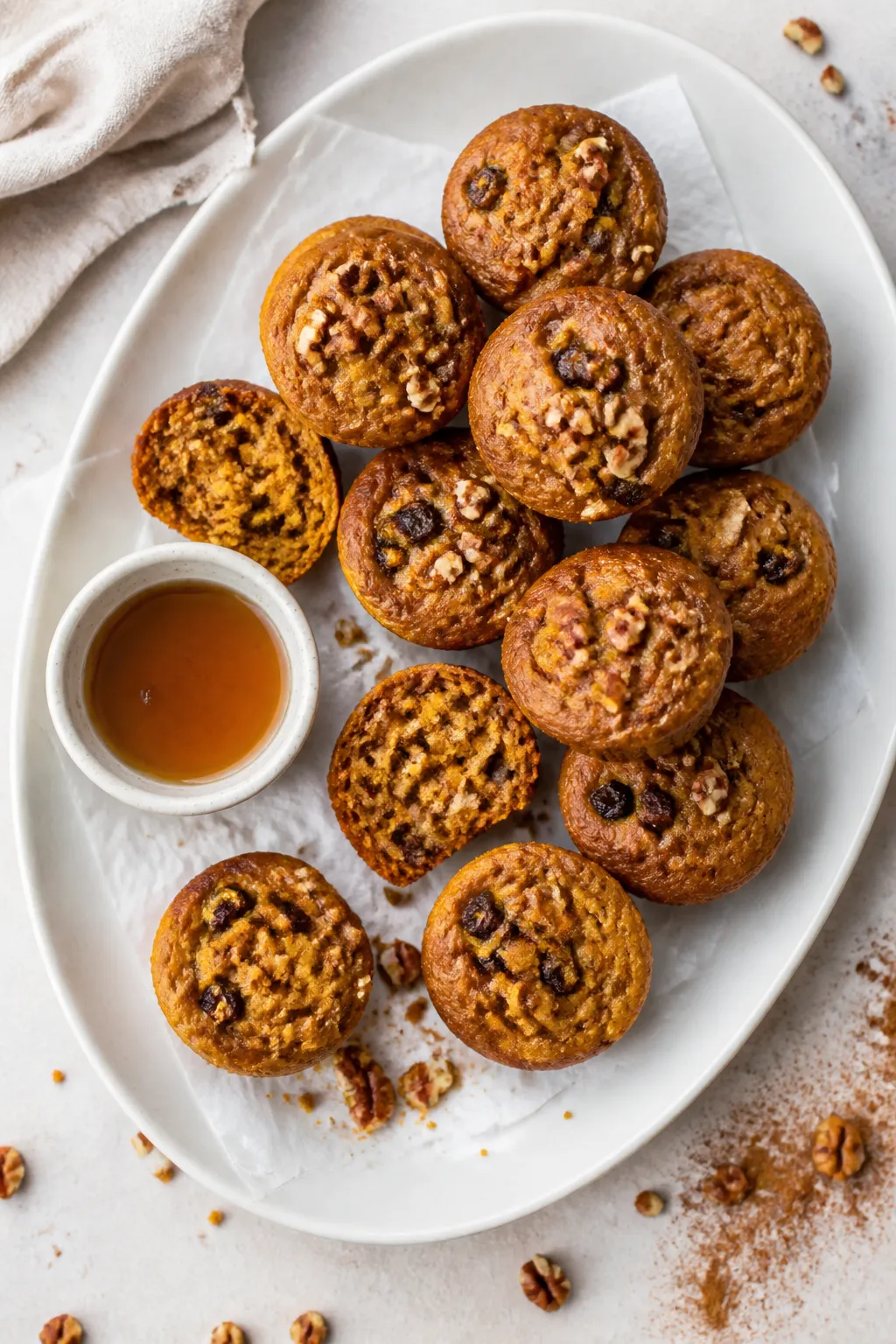 Overhead final presentation of mini pumpkin muffins on a matte white platter lined with parchment, a