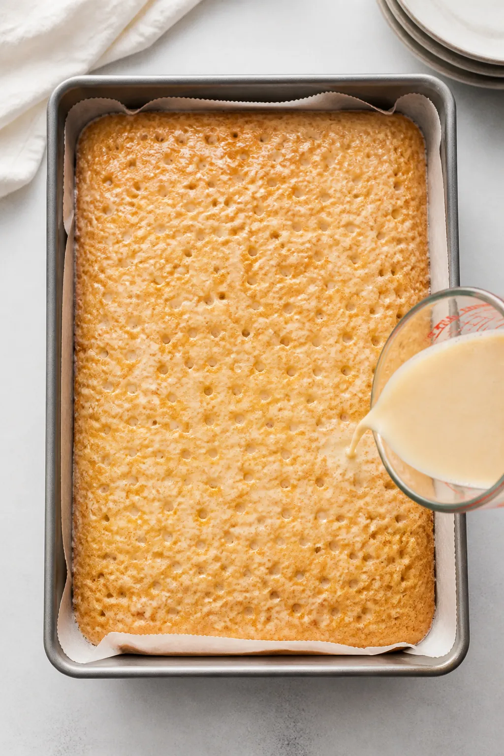 Overhead shot of a freshly soaked strawberry tres leches cake in a 9x13 pan: golden sponge pierced w