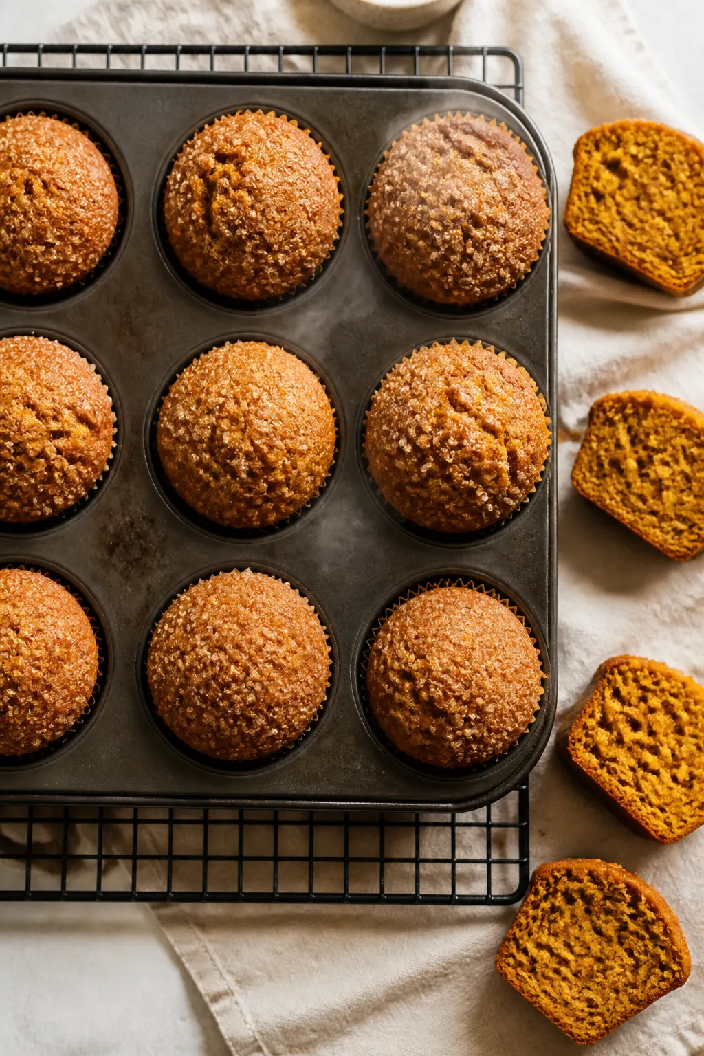 Overhead shot of freshly baked pumpkin muffins with domed tops cooling in a muffin pan on a wire rac